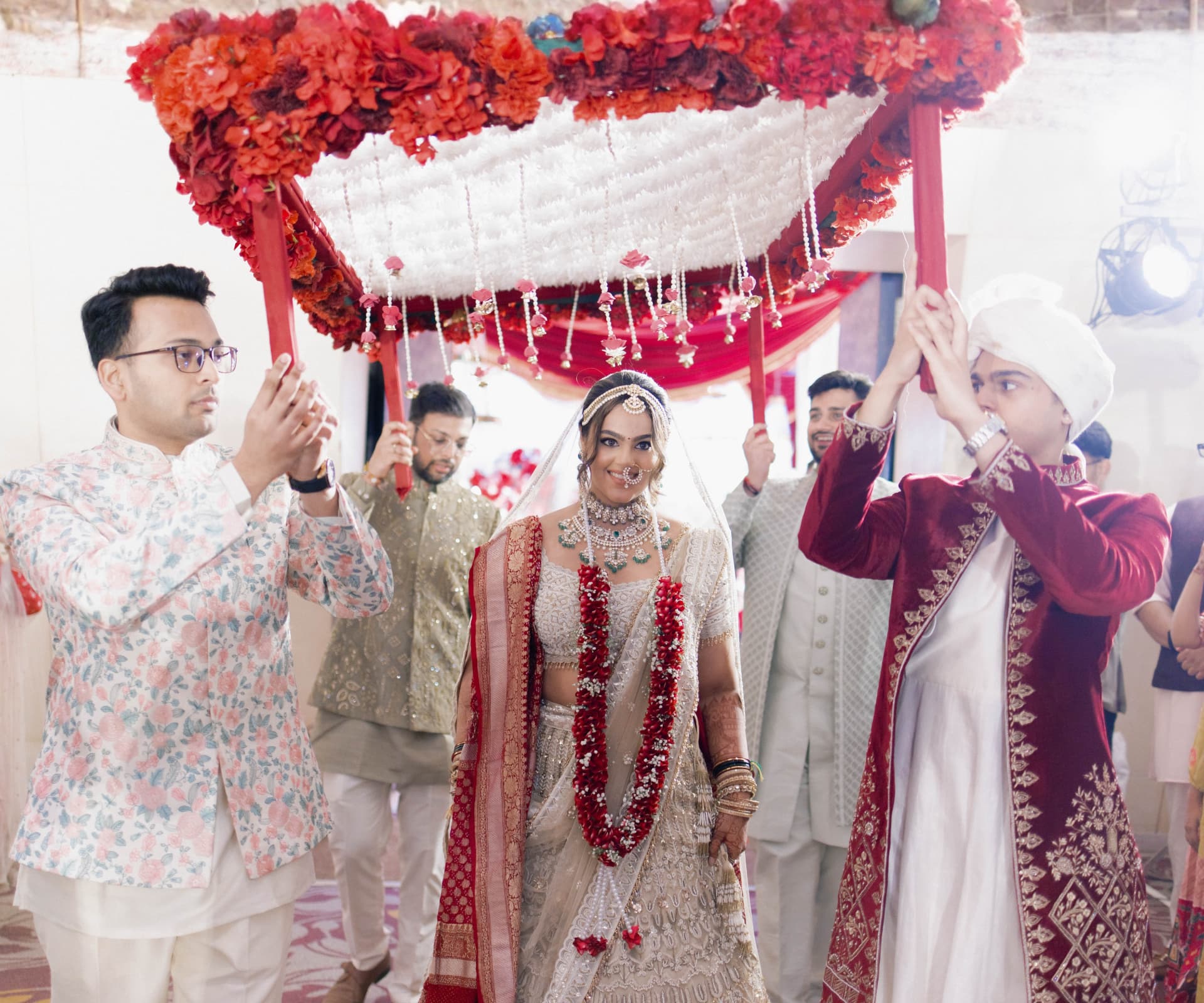 Bride in traditional Indian wedding attire beneath a floral phoolon ki chadar canopy